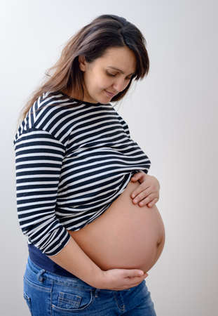 Cute expecting young woman with long hair in black and white striped shirt holding belly and grinningの写真素材