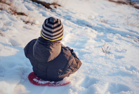 Small child sledding down a snowy slope in winter sunshine enjoying the fresh white snow and cold...