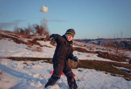 Small boy tossing a snowball at the camera as he plays outdoors in a snowy winter field