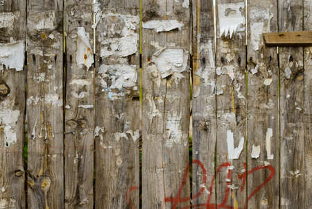 Rough worn out old wooden plank fence background with torn off posters and red spray paint graffiti and rusty nailsの写真素材