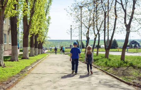Little boy and girl walking away from the camera down an avenue lined by trees on a sunny spring day