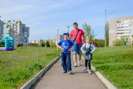 Young father with two children, a happy grinning young boy and girl, going for a walk along a path through a green lush urban parkの写真素材