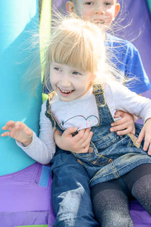 Adorable young brother and sister going down outdoor inflatable bouncy slide in purple and blue
