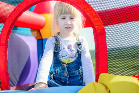 Cute little happy girl laying down on top of blue, red and yellow inflatable outdoor bouncy carnival amusement slideの写真素材