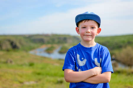 Happy attractive confident young boy in a trendy blue outfit standing with folded arms grinning at...