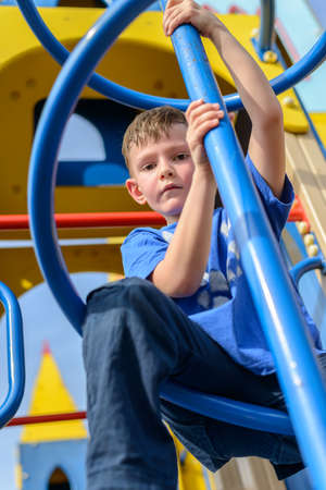 Low angle view on little boy in blue shirt and pants climbing twisted pole on play castle with blue sky behind himの写真素材