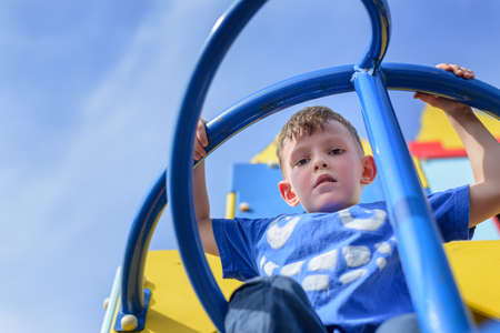 Low angle view on little boy in blue shirt and pants climbing twisted pole on play castle with blue sky behind himの写真素材