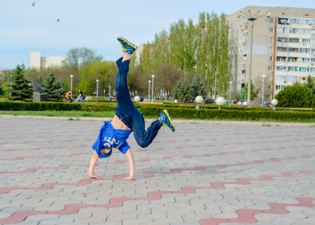 Agile young boy in a trendy blue outfit doing cartwheels in a paved urban square balancing on his...