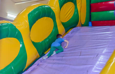 Little boy sliding down a slide in a bouncy castle on his stomach with a happy smile as a little...