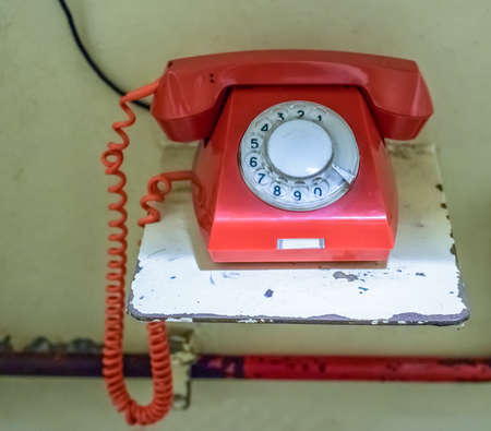 Old retro red emergency rotary telephone on a metal shelf reserved for important and urgent...