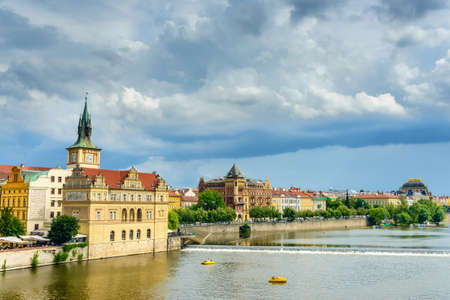 View of famous tall clock tower behind historic buildings from river with small dam and boats nearbyのeditorial素材