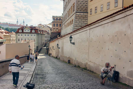 Elderly woman busking in an old cobbled street amongst historic urban buildings as a man walks by on the sidewalkのeditorial素材