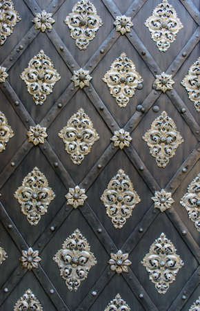 Door with an ornate metal motif in a repeat pattern in a geometric diamond frame on black wooden...