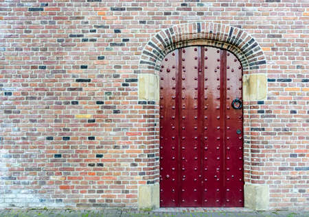 Old medieval red studded wooden door in a brick wall with variegated colors of brick in an architectural backgroundの写真素材