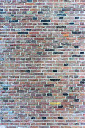 Background texture of a red brick wall interspersed with the odd black and yellow brick in a full frame vertical viewの写真素材