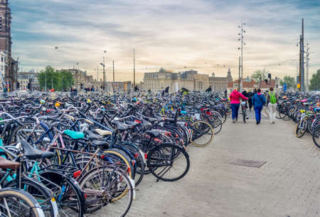Amsterdam, The Netherlands - 28 July 2016:Urban bike parking lot with hundreds of parked bicycles in assorted designs and people walking away towards the town in an eco friendly transport conceptのeditorial素材