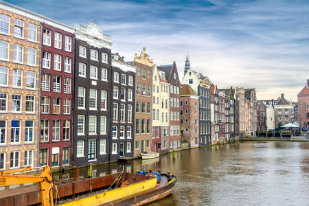 Amsterdam, The Netherlands, Scenic view of European city against river with boats docked nearby under a blue skyの写真素材