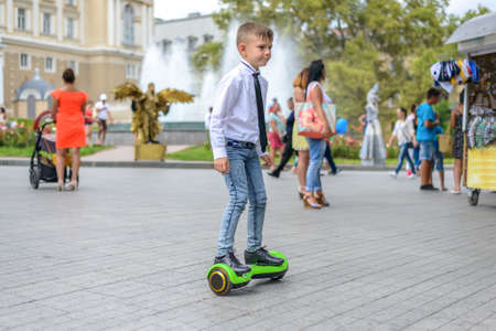 Stylish young boy riding a hover board in an urban park standing balancing on it facing the camera with a smileの写真素材