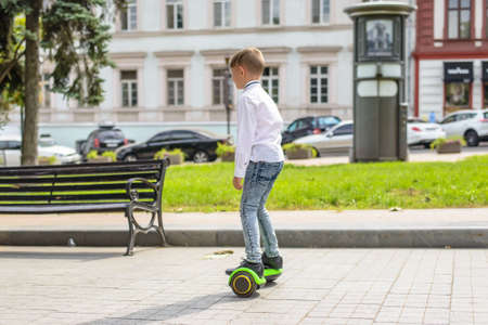 Stylish young boy riding a hover board in an urban park standing balancing on it facing the camera with a smileの写真素材