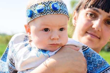Cute little baby girl in a pretty blue outfit with head band held in the arms of her loving mother, close up portraitの写真素材