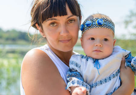 Adorable curious little baby girl peering at the camera with a pensive expression as she is held in her mothers armsの写真素材