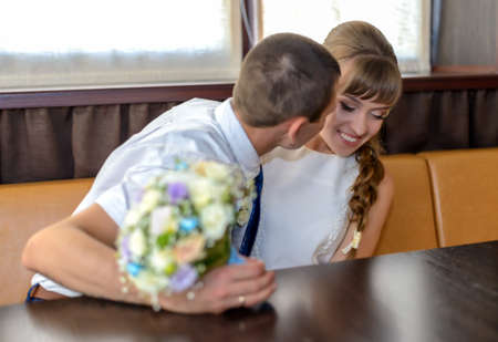 Enthusiastic husband bites the nose of his wife as they sit at a corner booth and while he holds a bouquetの写真素材
