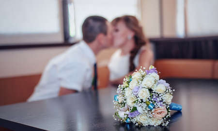 Selective focus of bridal bouquet on wood table as romantic newlyweds sit at booth by windowsの写真素材