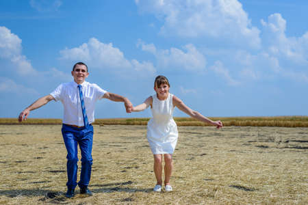 Happy young newlywed couple on a field running and jumping hand hand with joy as they celebrate their recent weddingの写真素材