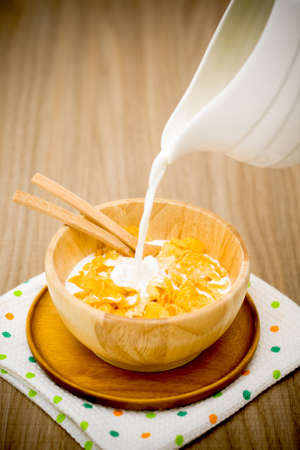 Milk pouring into a wooden bowl of nutritious and delicious corn flake cereal on wooden table. Darken effect.の写真素材