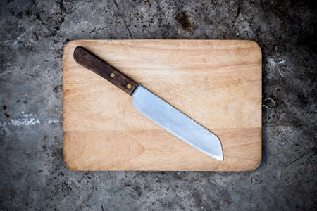 Empty chopping board with a sharp paring knife on a distressed grunge table in a rustic kitchen, overhead view with a vignette and copyspaceの写真素材