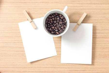 Top view of paper or cardboard with clothes pegs and coffee bean in coffee cup on wooden background....
