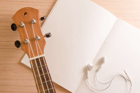 Ukulele, white earphones and paper or book on wooden backgroundの写真素材
