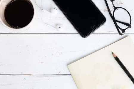 surface of a wooden table with notebook, smartphone, eye glasses, and pencil, top view