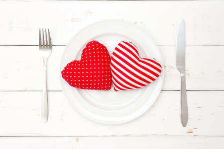 Red hearts on plate, fork and knife on wooden background