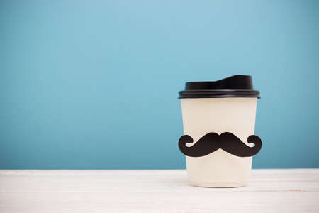 Take away coffee cup with hipster mustache on wooden table over blue backgroundの写真素材