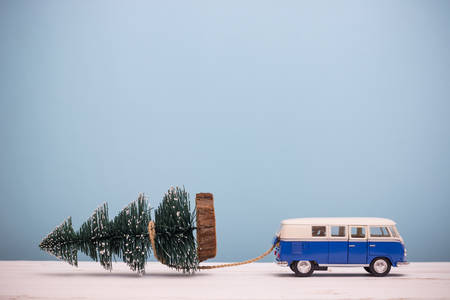 Miniature figure toy car drag Christmas tree on wooden table blue background, Image for Christmas Holiday decorative concept.の写真素材
