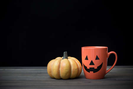 Coffee cup as jack o lantern pumpkin on wooden table. Halloween conceptの写真素材