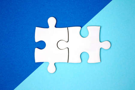 Two puzzle pieces connect on blue geometry color paper. Minimal style. Flat lay. Symbol of association and connection. business strategy.の写真素材