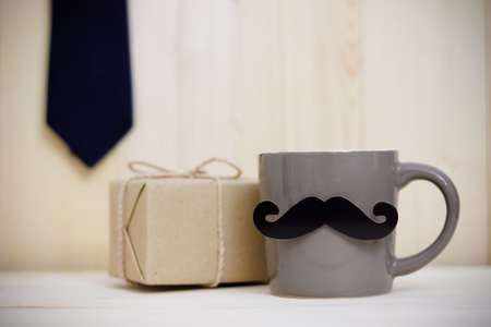 Tie, gift box, paper mustache, coffee cup on wooden background with copy space. Greetings and presents. Happy Father's Day.の写真素材