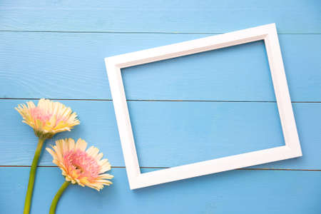 Photo frame and yellow flower on bright blue wooden background with petals. Summer flat lay.の写真素材