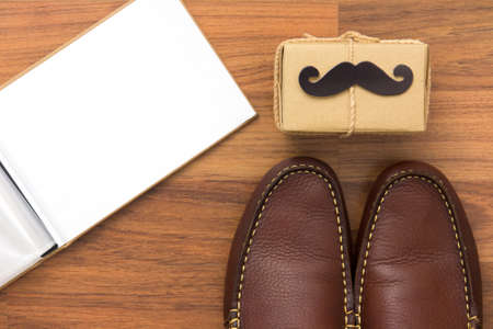 Gift box, paper mustache, shoes, photo book on wooden background with copy space. Greetings and...