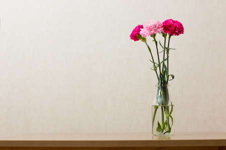 Pink carnation flowers in clear bottle on old woodの写真素材