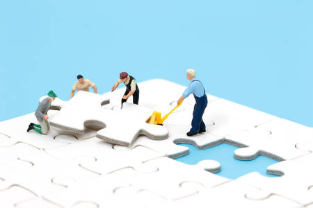Group of miniature people assembling jigsaw puzzle, team support and help concept. Business teamwork concept.の写真素材