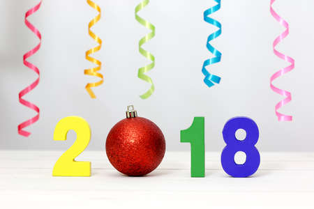 New Year 2018 is coming concept. Colorful wooden number, red bauble and ribbon on white table.の写真素材