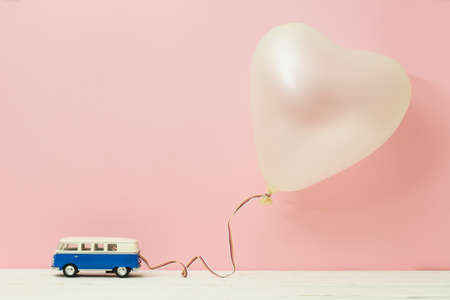 Miniature figure toy car drag balloon heart shape on wooden table pink background. Love and valentine day concept.の写真素材