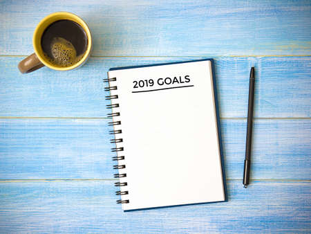 Top view of notebook handwriting goals for 2019 year, cup of coffee on blue wooden table. Business plan concept.の写真素材