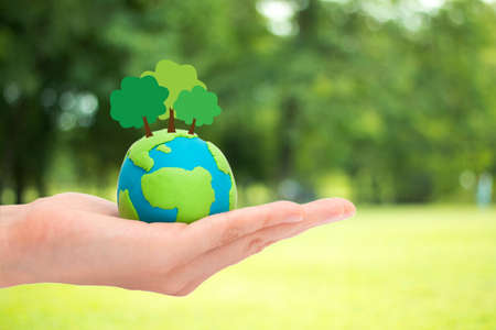 Human hands holding plant trees on the globe, planet or earth over blurred green garden nature background. Ecology concept.の写真素材