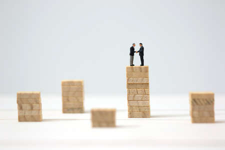 Miniature businessman cooperate on highest wooden stacks. Success, Dealing, Greeting and Partner concept.の写真素材