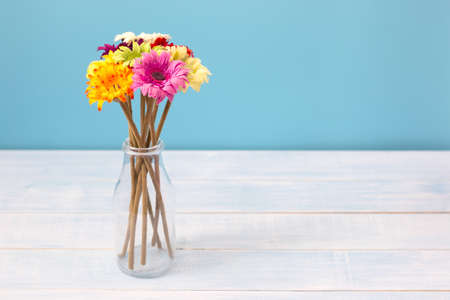 Colorful flowers bouquet in clear bottle on light blue table in front of blue wall. View with copy spaceの写真素材