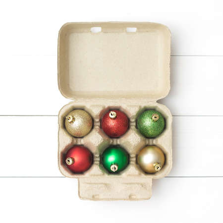 Christmas bauble decoration in brown carton egg box on white wooden background. Flat lay. Food idea...